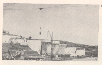 कोयना नदीच्या पात्रात एका बाजूचे धरणाचे बांधकाम चालू असतानाचे (दि. ७ एप्रिल १९६०) चित्र. चित्रामध्ये आकाशरज्जू मार्गाने काँक्रिट मिश्रण योग्य ठिकाणी टाकण्याचे पात्र आणि यारी दाखविलेली आहे.